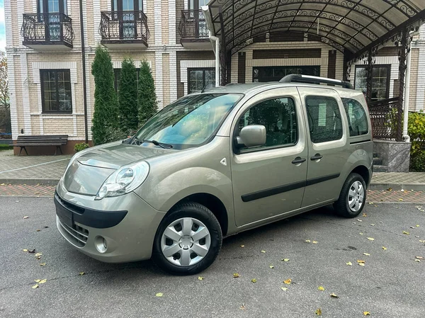 Büyük bir binanın önünde bir araba park edilmiş. Olay yeri, yakınındaki ağaçlar ve kapalı bir girişi olan açık bir günü gösteriyor. Binanın birkaç katı ve penceresi var..