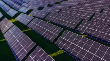 Güneş panellerinin sıraları parlak yeşil bir manzara boyunca uzanıyor, güneş ışığını emiyor. Bu sahne sürdürülebilirlik ve temiz enerji çözümleri üzerindeki artan odak noktasını vurgular.