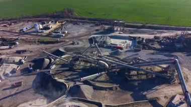 Makinelerle ve taşıma bantlarıyla dolu inşaat alanı taşları çıkarmak ve işlemek için çok çalışıyor. Çevreleyen yeşil alanlar bu güneşli atmosferde çarpıcı bir kontrastlık yaratır..