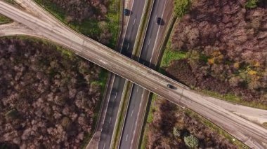 Araçlar yeşil ve kahverengi ağaçlarla çevrili bir otoyol kavşağında ilerliyorlar. Görüntü, bölgede birleşen yolların genel görünümünü gösterir..
