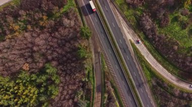 Kamyonlar ve arabalar yeşil ağaçlar ve bazı kahverengi bölgelerle çevrili bir otoyolda seyahat ediyorlar. Önünde gözle görülür bir engel olmadan aydınlık ve berrak..