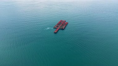 Denizde yüzen bir midye çiftliği görülüyor. Yapılar çiftçilik için midye tutar. Su çiftliği çevreledi. Görünürde tekne ya da insan yok. Gökyüzü bulutsuz berrak.