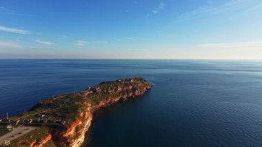 Okyanusa doğru uzanan kayalık bir kıyı şeridi, suyun üzerinde yükselen kayalıklar. Gökyüzü açık ve mavi, gün ışığını gösteriyor. Dalgalar usulca kıyıya doğru ilerliyor..