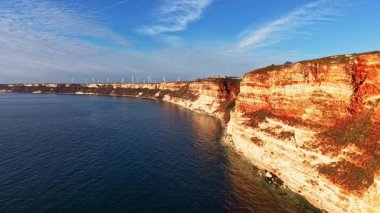 Rüzgar türbinleri uzaklıktan görülebildiği için uçurumlar denizin üzerinde dik duruyor. Kıyı şeridine yakın güneşli bir günde gökyüzü bulutları gösteriyor..