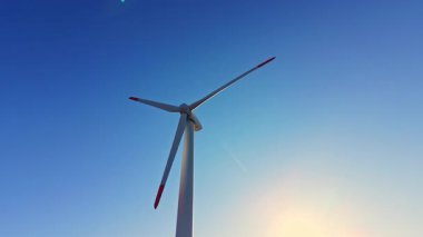 Rüzgar türbini gün ışığında elektrik üretirken yavaşça dönüyor. Açık gökyüzü yenilenebilir enerji üretimine ekleniyor.