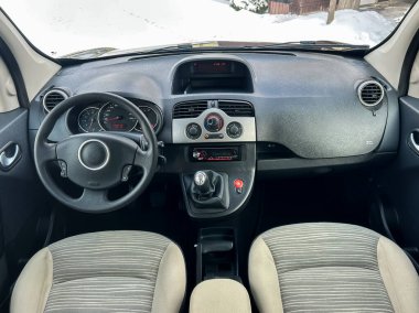 Arabanın içi gösterge paneli, direksiyon simidi ve vites kolunu gösteriyor. Araba karlı bir bölgede. Kontroller zamanı gösteren sayıları gösteriyor. Koltuklar hafif renklidir..