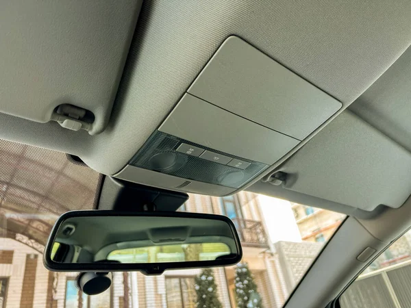 Tepedeki konsol ve dikiz aynası park halindeki bir arabanın içinde görünür. Işık arabaya giriyor, yerleşim alanının bir kısmını bazı binalarla birlikte gösteriyor..