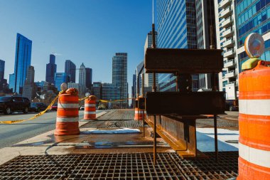 İşçiler bir şehir merkezinde inşaat işiyle meşgul. Trafik, güneşli bir günde açık mavi gökyüzüne karşı arka planda yüksek binalar bulunan güvenlik konileri tarafından tıkandı..