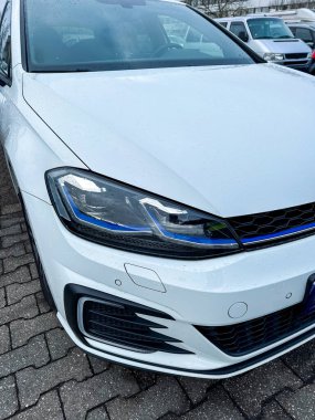 Araba bulutlu gökyüzünün altında park halinde. Su damlacıkları yüzeyde ve ön taraf temiz. Bu ayarda yakınlarda başka araç yok..