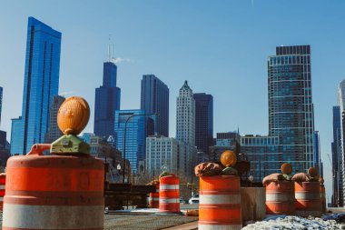 Şikago 'da bir şehir yolunda inşaat devam ediyor. Bölgeye trafik bariyerleri ve uyarı ışıkları kuruldu. Açık bir gökyüzünün altında arka planda uzun binalar görülebilir..