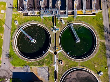 Bir su arıtma tesisinde iki dairesel tank görülebilir. Makineler ve boru hatları tankların etrafını sardı. Konumu yeşil çim ve asfalt manzaralı kentsel.