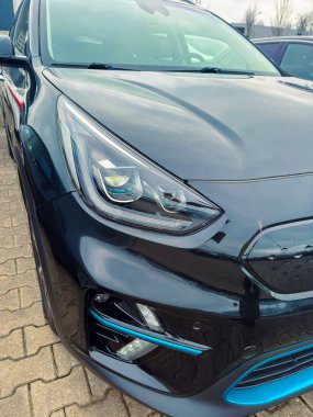 Yakından bakınca, parlak farları ve kendine özgü ızgarası olan modern bir arabanın önünü görüyoruz. Sahne bulutlu bir günde bir otoparkta geçiyor. Yakınlarda birkaç araba var..