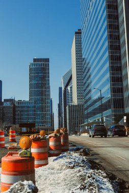 İşçiler yüksek binalarla dolu bir caddeye gün boyunca inşaat bariyerleri kurdular. Ufuk çizgisi iş alanının üzerinde görünürken araçlar geçiyor..