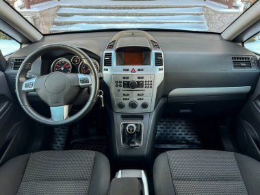 Arabanın içi, gösterge paneli, direksiyon ve koltukları net bir şekilde görülebilir. Pencerenin dışında kar görünüyor, soğuk havayı gösteriyor..