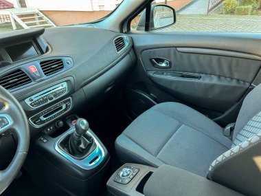 Arabanın içinde kontrol paneli, direksiyon simidi ve ön yolcu koltuğu bulunur. Güneş ışığı araca vuruyor, temiz bir alan gösteriyor..