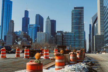 İşçiler Şikago şehir merkezinde bir caddede inşaatta çalışıyorlar. İnşaat konileri yol boyunca dizildi. Açık mavi gökyüzünün altında arka planda yüksek binalar yükselir..