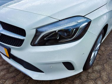 Yağmur sırasında beyaz bir araba bir otoparkta park edilir. Su damlacıkları yüzeyi kaplıyor ve arabada ışıktan yansımalar görülebiliyor. Sahne sıradan bir günü gösteriyor..