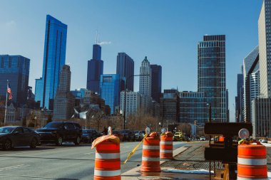 İşçiler Chicago 'da bir şehir caddesinde inşaat yapıyorlar. Trafik inşaat engellerini aşıyor. Açık mavi gökyüzünün altındaki yüksek binalar gökyüzünü dolduruyor..