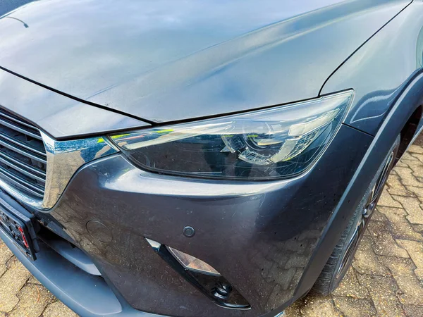 Tuğla yüzeyde gri bir araba duruyor. Ön far pırıl pırıl parlıyor. Görüntü kaputun detaylarını ve arabanın çizgilerini yakalıyor..