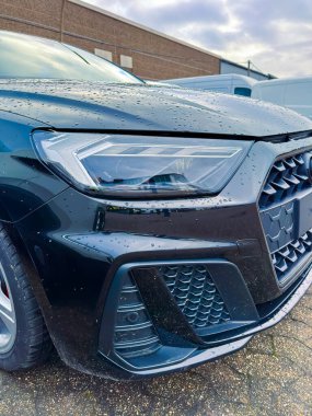 Siyah bir araba bir binanın yanında park edilmiş. Yağmur damlaları, ıslak bir bakış göstererek arabanın yüzeyini kaplıyor. Sahne öğleden sonra gökyüzünde bulutlarla başlar..