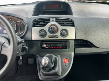 Gösterge paneli bir arabanın klima kontrol panelini ve radyo sistemini gösteriyor. Vites kolu kontrollerin yanında görünüyor. Zaman göstergesi geçerli saati gösterir.