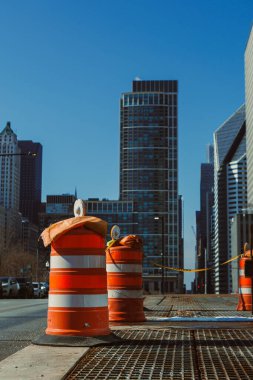 İşçiler aydınlık bir günde, inşaat alanında araçlara rehberlik etmek için turuncu trafik varilleri kurdular..