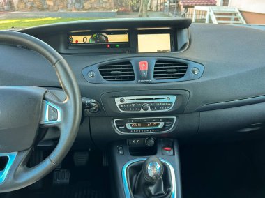 Bir arabanın kontrol paneli, ses ve iklim ayarları için kontroller, ekranlar ve düğmeler. Dışarıda güneş ışığı görünen açık bir gün..