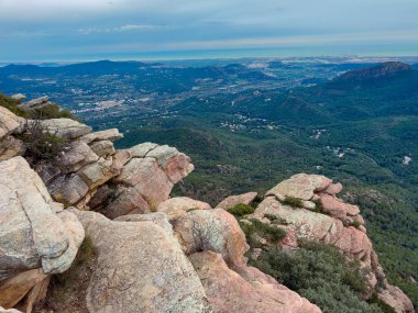 Vadinin yukarısındaki kayalıklar şehri ve suyu gösteriyor. Yeşil ağaçlar tepeleri kaplıyor. Bulutlar gökyüzünü dolduruyor. Bu sahne doğa ve şehir yaşamını bir arada yakalar..