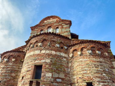 Yuvarlak bir yapısı ve tuğla duvarları olan bir kilise mavi bir gökyüzünün altında duruyor. Bina, pencere ve taşların detaylarını gösteriyor. Yunanistan 'da tarihi mimarinin bir örneği..