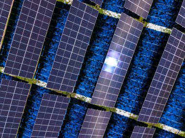 Güneş panellerinin sıraları yukarıdan görülür ve geniş bir alana yerleştirilir. Paneller doğrudan güneş ışığı alıyor, kirlilik olmadan elektrik üretme amaçlarını gösteriyor..