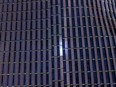 Geniş bir güneş paneli düzeni açık gökyüzünün altında görülebilir. Güneş pilleri güneş ışığını yansıtarak, yenilenebilir enerji toplama ölçeğini gösterir.