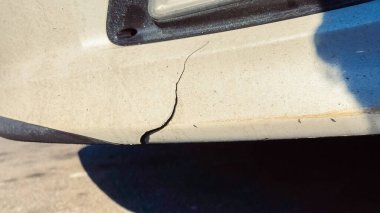 Caddeye park etmiş bir araba tamponunun alt kısmında görünür bir çatlak gösteriyor. Günün ışığı hasarı ayrıntılarıyla vurguluyor..