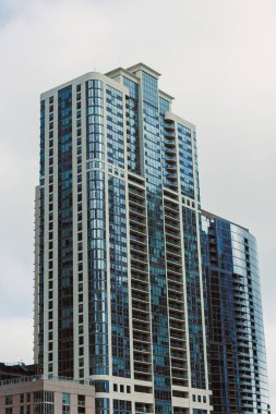 Şehirdeki yüksek bir apartman gri gökyüzüne karşı duruyor. Birçok pencere ve balkonu olan modern bir tasarımı gösteriyor..