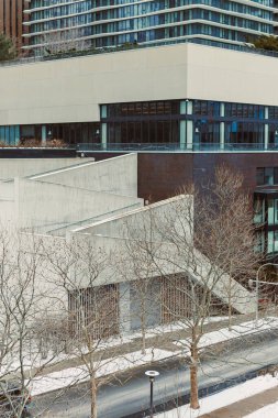 Somut yapı, temiz bir gökyüzünün altında ağaçların dizildiği bir şehir sahnesinde cam cephelerle kesişiyor.