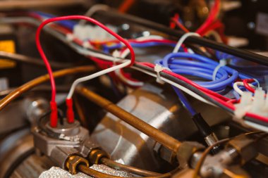 Kırmızı, beyaz ve mavi kablolar bir makinenin içindeki metal bileşenlere bağlıdır. Görüntü, endüstriyel bir yapıdaki kabloların ve bağlantıların yakın çekimini gösteriyor..