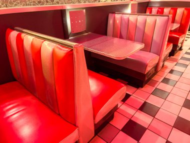 Boş yemek odalarında restoranda masası olan kırmızı ve mor kabinler bulunur. Zeminde kareli bir desen var ve ayarı yumuşak renklerle aydınlatılmış..