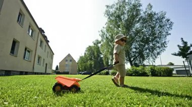 2 yaşında şortlu bir çocuk ve kafasında Panama şapkası olan bir çocuk sokakta yürüyor ve tasmalı bir arabayı çekiyor. Bebek parkta yürürken bir arabayı ipten çekip çıkartıyor. Sokaklar için çocuk oyuncakları