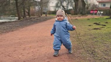 Sokakta yürüyen, 1 yaşında, tulumlu bir çocuk. Çocuk temiz havada yürüyüşe çıkmış. Çocuk parkında sonbahar yürüyüşü.