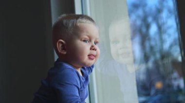 1 yaşında bir çocuk pencere pervazında dikiliyor ve pencereden dışarı bakıyor. Çocuk pencereden sokağa bakıyor..