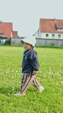 Kafasında panama şapkası olan 2 yaşındaki bir çocuk şehir parkında yeşil çimlerde koşuyor. Yazın yürüyüşe çıkmış küçük bir çocuk. Çocuklar için şık kıyafetler. Pantolonlu bir çocuk ve sokakta bir bluz..