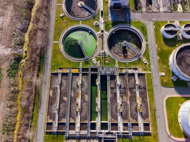 İşçiler, su arıtma tesisinde kullanılan çoklu büyük yuvarlak ve dikdörtgen tankları yönetiyorlar. Site atık su işleyerek çevresel güvenliği ve uyumu sağlar.