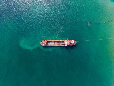 Bir kargo gemisi temiz mavi suyun üzerinde duruyor, kargo operasyonlarını yöneten işçiler var. Ekipman teknenin yanında kullanılıyor ve güneşli bir günde tepemizde parlıyor..