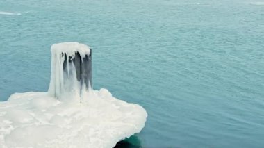 Bir su kütlesinin kenarında buzla kaplı ahşap bir direk görülür. Su mavi ve soğuk görünüyor, kışın tutuşunu gösteriyor. Sahne sessiz ve durgun, kışı çağrıştırıyor..