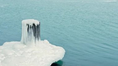 Buzla kaplı ahşap bir iskele buzlu mavi tonları olan suyla kaplıdır. Sahne, buz ve su arasındaki zıtlığı gösteren gölün kıyısında soğuk bir kış günü tasvir ediyor..