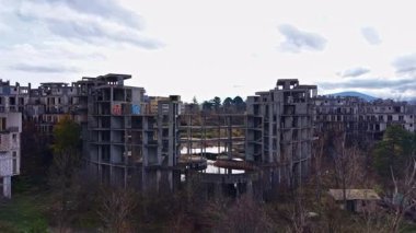 Yıkılan beton yapılar, bir zamanlar canlı olan duvarları artık solmuş ve büyümüş olan sakin bir göletin etrafını sarıyor. Doğa bu unutulmuş yeri geri alır. Bulutlar yavaşça tepemizde sürüklenirken..