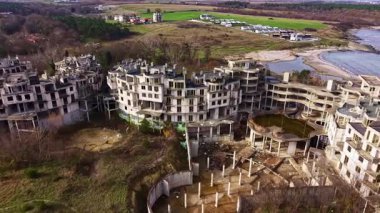 Terk edilmiş yapılar kıyı şeridi boyunca uzanır, eski yapıların kalıntılarını gösterir. Yabani otlar ve ağaçlar beton içinde büyür, doğayı insan çabalarıyla harmanlarlar. Huzurlu arka plan kayıp rüyaları ima eder..