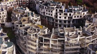 Yıkılan binalar, doğa alanı geri almaya başlarken dağınık bir şekilde duruyor ve sakin bir manzaranın ortasında terk edilmiş bir mimari projeyi vurguluyor..