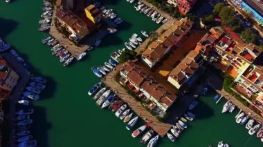 Güneşli bir günde kıyı kasabasında birkaç tekne, binalarla çevrili marinalarda rıhtıma yanaşır. Su, güneş ışığını yansıtır ve liman yakınlarında günlük yaşamın canlı bir sahnesini yaratır..