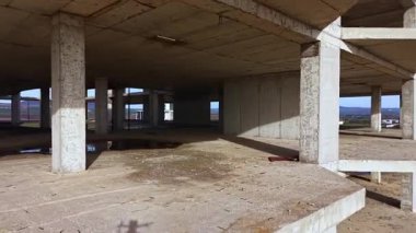 Bitmemiş beton sütunlar ve geniş açık alanlar, doğanın ve ihmalkarlığın alacakaranlığın yumuşak renkleri altında iç içe geçtiği sahneye hükmediyor. Geçmişteki hırsların yankıları havada duruyor..