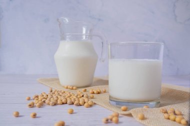 Lezzetli organik soya sütünü cam bardakta ve soya fasulyesinde veya cam kasedeki soya fasulyesini ahşap masa zemininde kapat. Soya sütü soya sütünden yapılan bir içecektir. Alternatif süt ve sağlıklı bir kavram..
